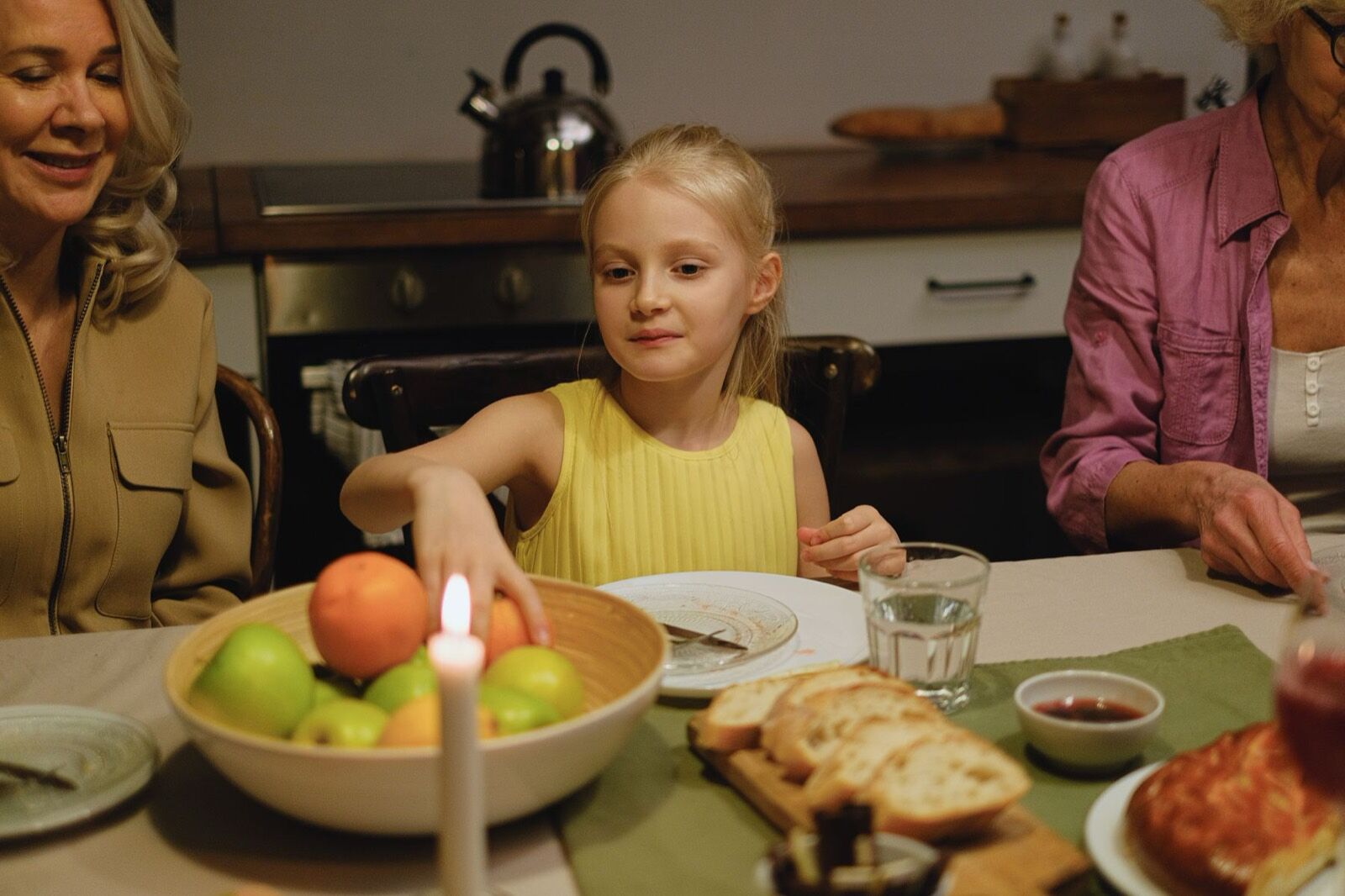 A girl at a candlelit family dinner table between her mother and grandmother